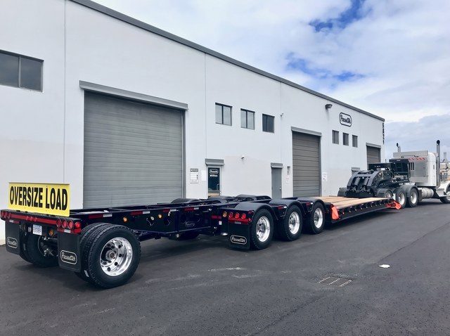 Black lowbed with blue trim and a pin-on booster behind the Oversize Load sign.