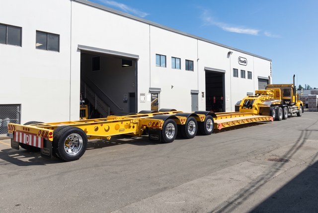 Rear three-quarter view of the yellow lowbed and booster behind the matching tractor.