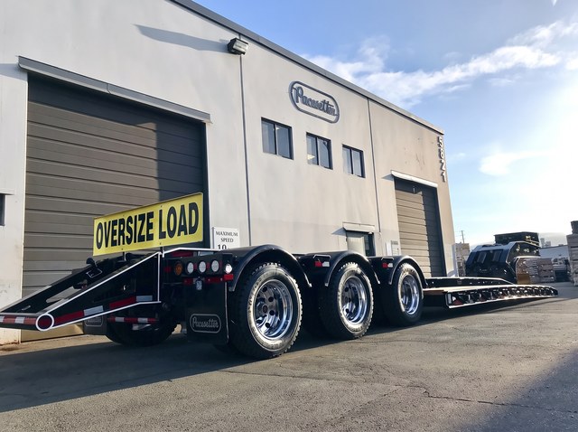 Rear three-quarter view of the black lowbed with white trim and Oversize Load sign.