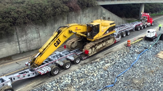 The white customer lowbed transporting an excavator on a highway job.