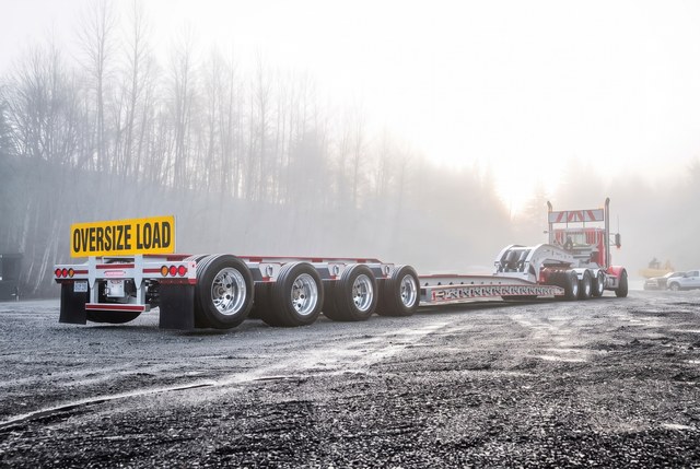 White customer lowbed at work in a gravel yard at sunrise.