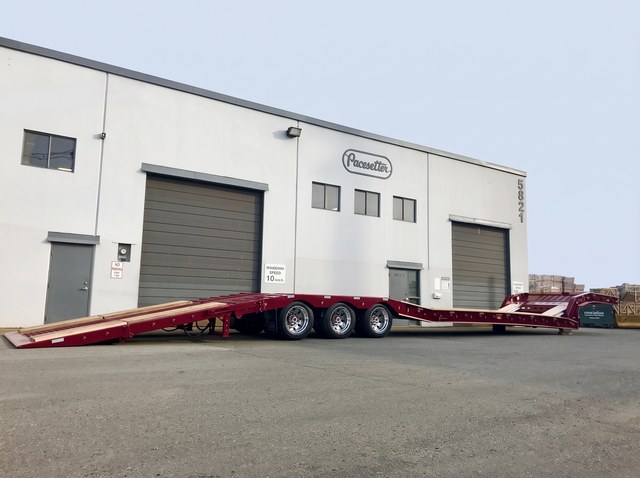 Burgundy paving trailer with its rear loading ramp lowered outside Pacesetter.