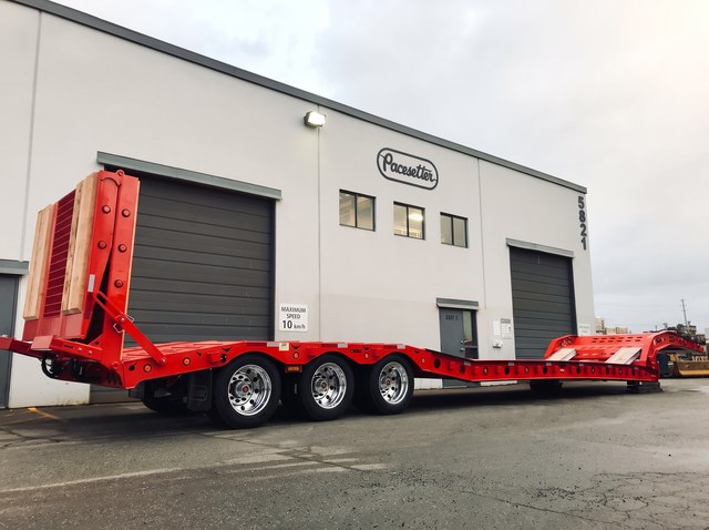 Red paving trailer with a raised rear loading ramp and three rear axles.