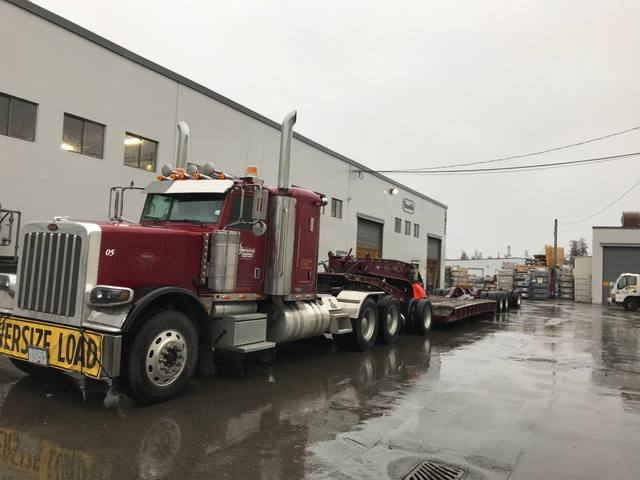 Burgundy 65 ton lowbed with matching Peterbilt tractor leaving the Pacesetter plant in the rain, photo 1 of 3